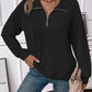 Woman wearing a black striped half zip long sleeve t-shirt with jeans and a beige handbag