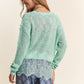 Woman wearing a J.NNA lace detail long sleeve knit top in mint green, showcasing intricate lace accents and elegant style.