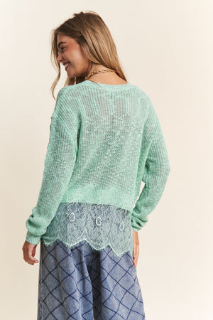 Woman wearing a J.NNA lace detail long sleeve knit top in mint green, showcasing intricate lace accents and elegant style.