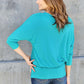 Woman wearing a turquoise Round Neck Batwing Sleeve Top with slightly stretchy fabric, shown from the back against a concrete wall.