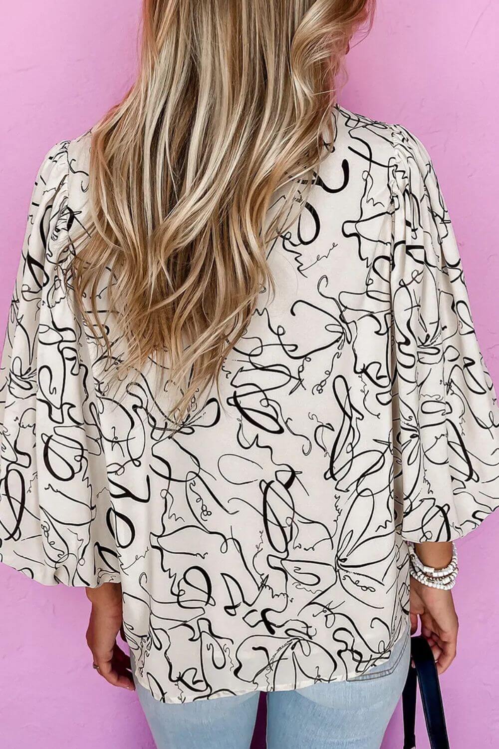 Woman wearing Bella Road printed round neck three-quarter sleeve blouse with abstract design, viewed from the back.