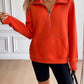 Woman wearing an Ivy Lane Half Zip Raglan Sleeve Sweatshirt in bright orange with black shorts, featuring a front pocket and zipper detail.