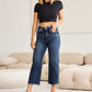 Woman wearing Tummy Control High Waist Raw Hem Distressed Jeans and black crop top standing in living room. RFM Jeans.