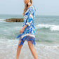 Woman wearing a blue cutout V-neck three-quarter sleeve cover up with tassels, walking on the beach.