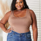 Woman wearing everyday full-size basic tank bodysuit paired with blue jeans, with a backdrop of neutral decor.