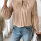 Woman wearing Perfee Frill Tie Neck Long Sleeve Blouse with ruffled details and lace accent, paired with jeans, holding a clutch.