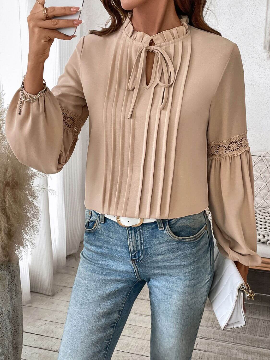 Woman wearing Perfee Frill Tie Neck Long Sleeve Blouse with ruffled details and lace accent, paired with jeans, holding a clutch.