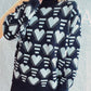 Woman wearing Bella Road Heart Contrast Long Sleeve Dropped Shoulder Sweater with black background and white hearts design.