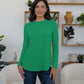 Woman wearing a green FAM-FAM round neck long sleeve t-shirt with decorative buttons, styled casually in a cozy room.