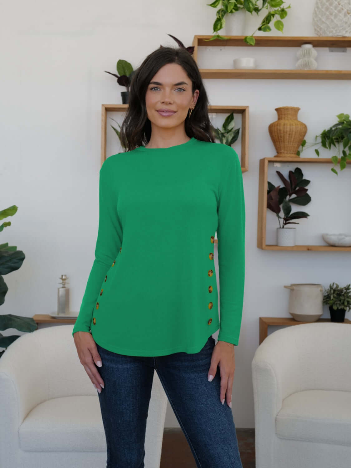 Woman wearing a green FAM-FAM round neck long sleeve t-shirt with decorative buttons, styled casually in a cozy room.