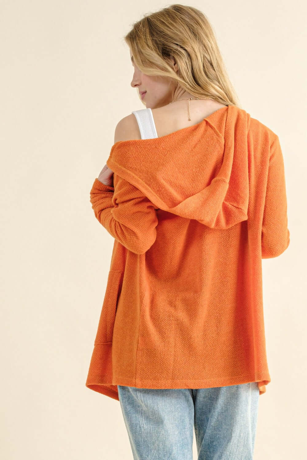 Woman wearing orange thermal hooded open front cardigan with pockets, showing back view with casual style and cozy fabric.