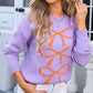 Woman wearing lavender Angel Wings Bow Graphic Round Neck Long Sleeve Sweater with orange bow designs, white hat, and white pants