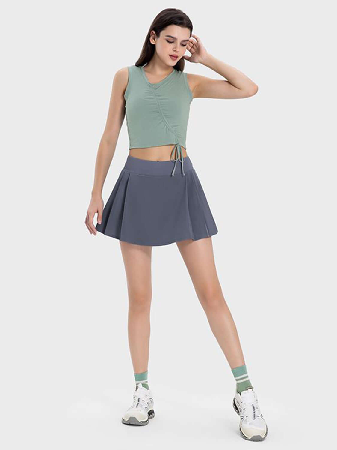 Model showcasing the Millennia Pleated Detail Mid-Rise Waist Active Skirt paired with a stylish top and sporty sneakers.