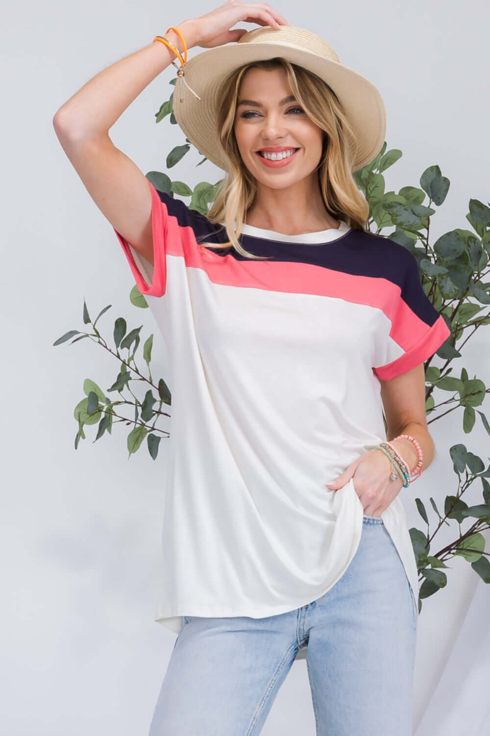 Woman wearing Color Block Round Neck Short Sleeve T-Shirt with red, white, and navy color blocks and jeans while smiling and holding a hat