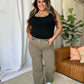 Woman wearing RFM Full Size High Rise Garment Dye Wide Leg Jeans with a black top, standing in a stylish living room with plants and a brown sofa