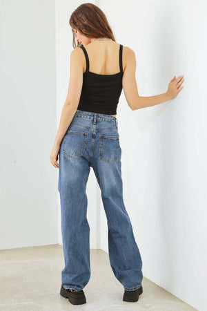 Woman wearing distressed high waist jeans with a black tank top, showcasing trendy and versatile denim style from the back.