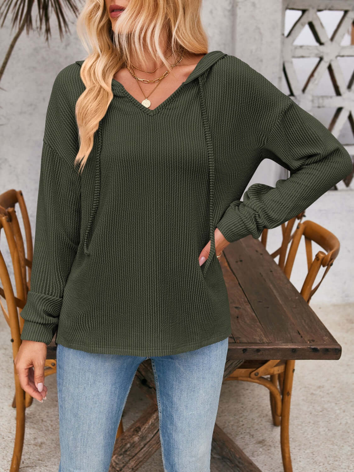 Woman wearing a drawstring dropped shoulder long sleeve hoodie in dark green, paired with light blue jeans, standing in casual outdoor setting.