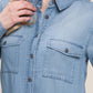 Denim shirt with scooped hem and button-up design, featuring front pockets and a classic collar, worn by a model.