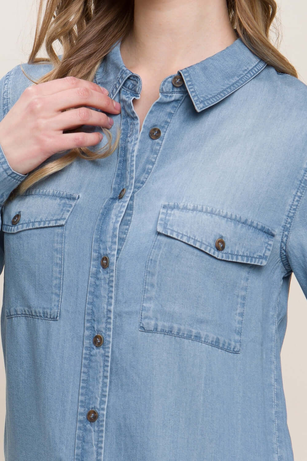 Denim shirt with scooped hem and button-up design, featuring front pockets and a classic collar, worn by a model.