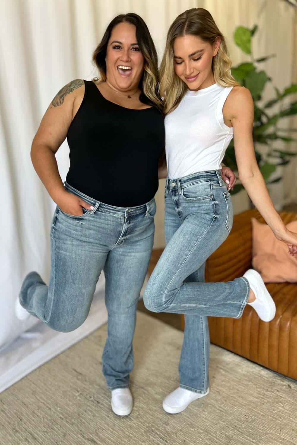 Two women wearing Judy Blue medium rise bootcut jeans, showcasing the comfortable fit and flattering style in a casual setting.