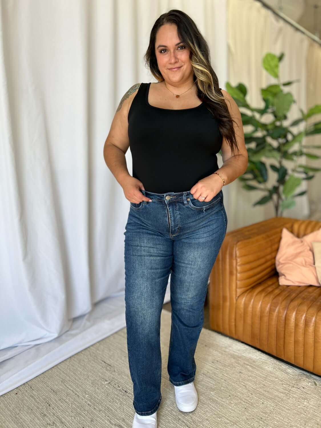 Woman wearing RFM Full Size High Rise Straight Tummy Control Jeans, standing indoors by a couch and plant