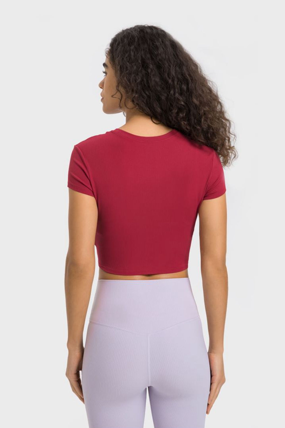 Back view of woman wearing Millennia Round Neck Short Sleeve Cropped Sports T-Shirt in burgundy with yoga leggings.