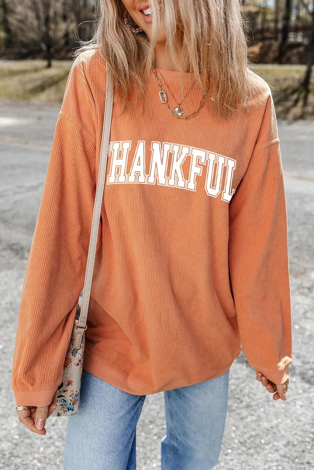 Woman wearing Bella Road THANKFUL round neck long sleeve sweatshirt in orange, styled with light blue jeans and a crossbody bag.