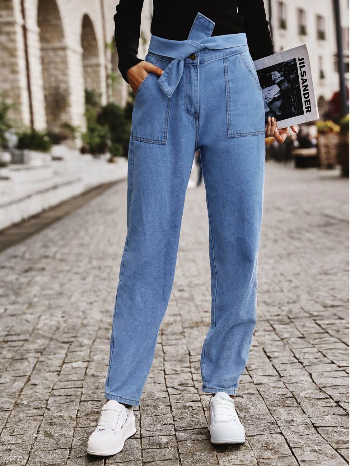 Stylish woman wearing Bella Road Tied Straight Jeans with pockets while holding a magazine on a cobblestone street