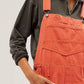 Woman wearing orange Bella Road Denim Overalls with wide straps and pockets, paired with a dark sweatshirt for a stylish look.