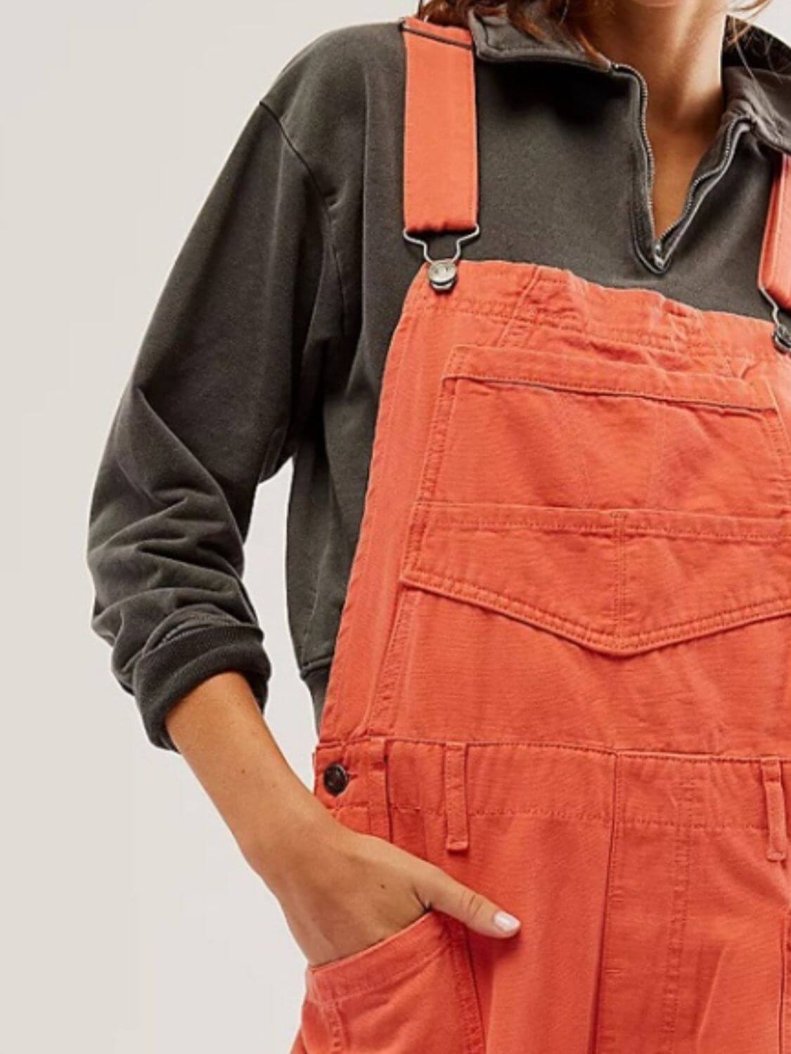 Woman wearing orange Bella Road Denim Overalls with wide straps and pockets, paired with a dark sweatshirt for a stylish look.