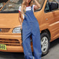 Woman wearing Bella Road wide leg denim overalls, posing confidently in front of an orange van. Fashion meets comfort.