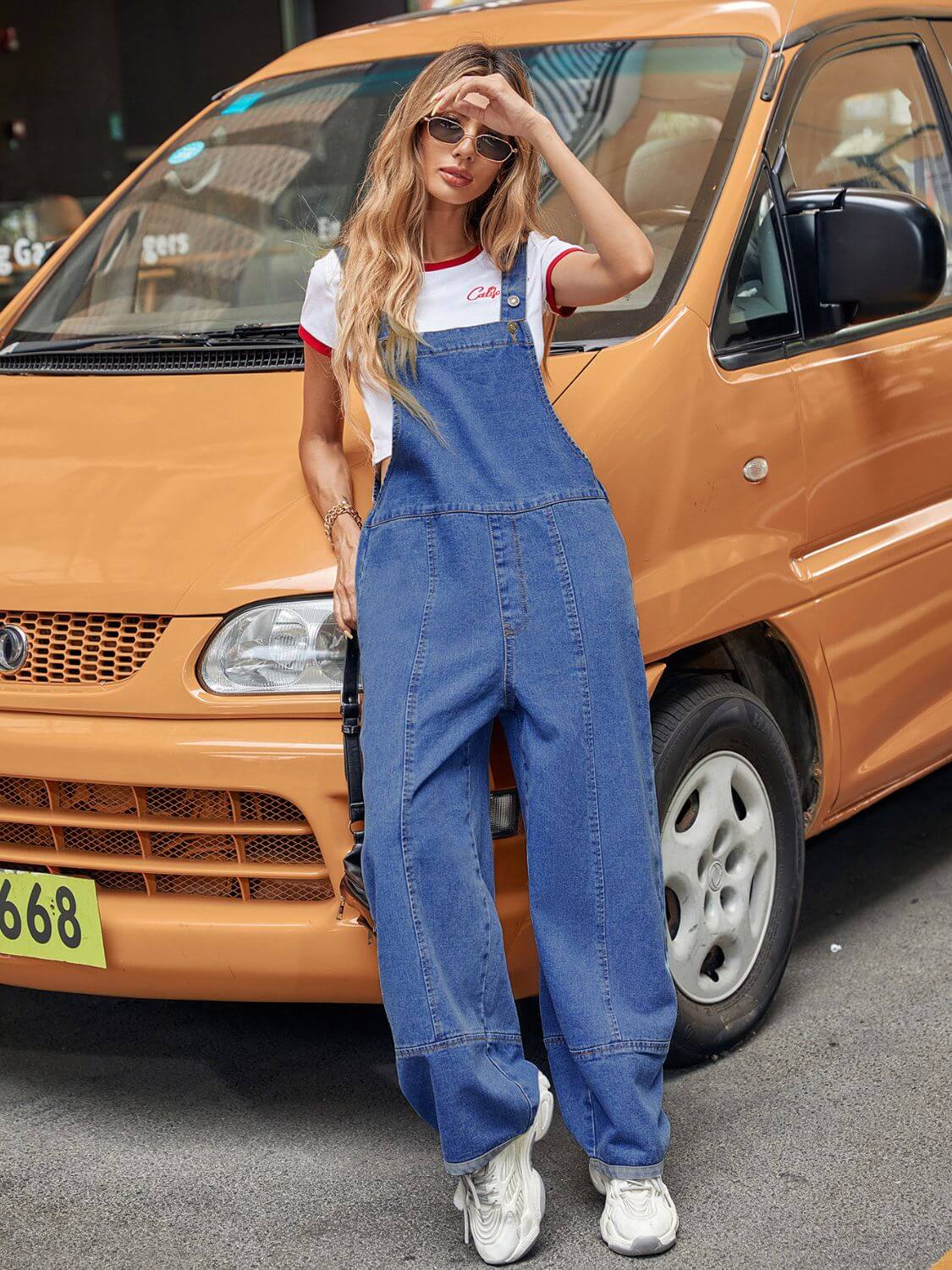 Woman wearing Bella Road wide leg denim overalls, posing confidently in front of an orange van. Fashion meets comfort.