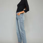 Woman wearing trendy high waist raw hem cropped wide leg jeans and black top standing against a gray background