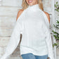 Woman wearing Bella Road Cable-Knit Turtleneck Cold Shoulder Sweater in white, showcasing trendy cut-out shoulders and cozy design.