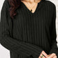 Woman wearing a black ribbed notched long sleeve top with slight stretch, showcasing the details of the fabric and neckline.