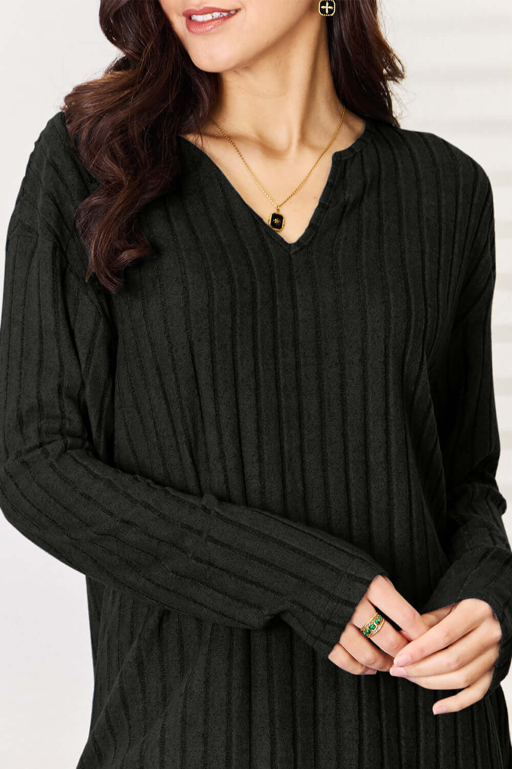 Woman wearing a black ribbed notched long sleeve top with slight stretch, showcasing the details of the fabric and neckline.