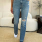 Woman wearing Mid Rise Destroyed Hem Distressed Judy Blue Jeans with white sneakers standing in a living room.