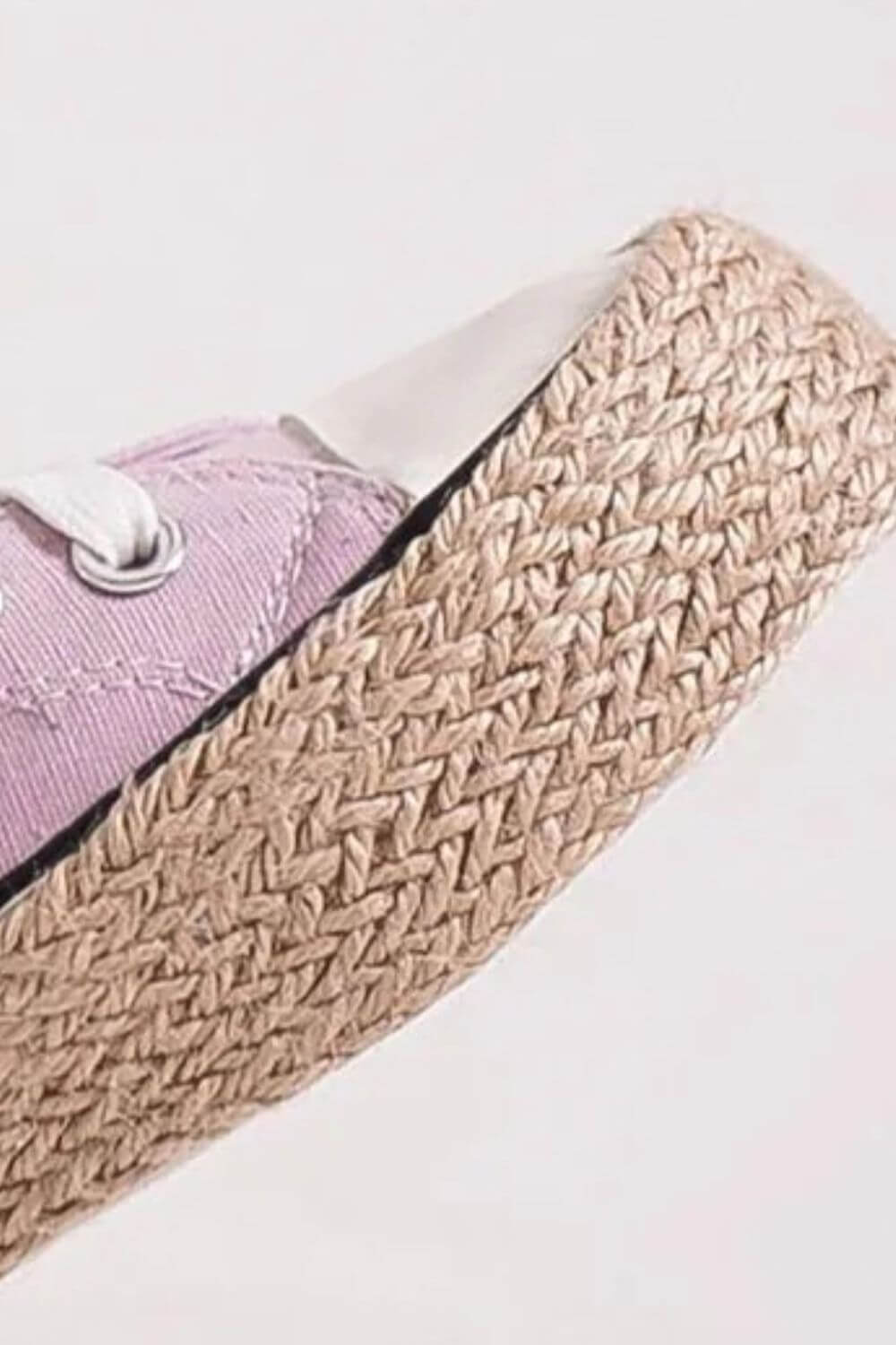 Close-up of a pink lace-up sneaker showcasing a stylish woven espadrille sole for a trendy summer look.