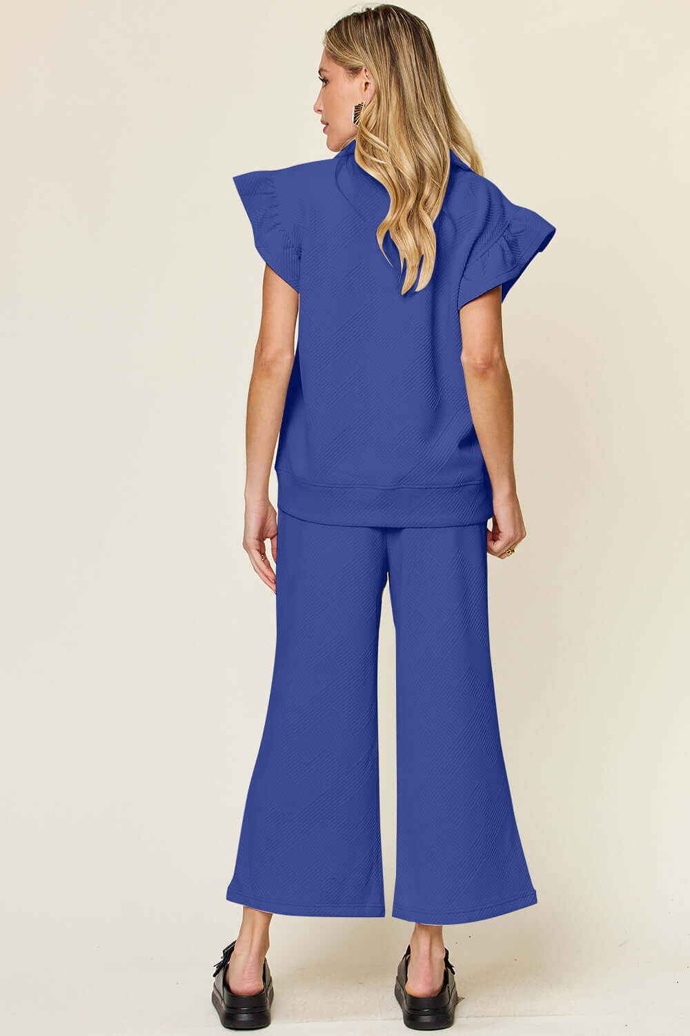 Woman wearing blue texture ruffle short sleeve top and drawstring wide leg pants set, back view.