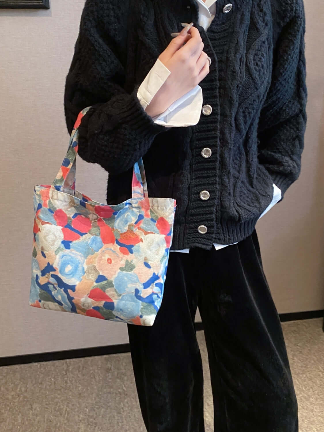 Woman holding printed canvas handbag with zipper, medium size, colorful floral design, black sweater, casual fashion accessory