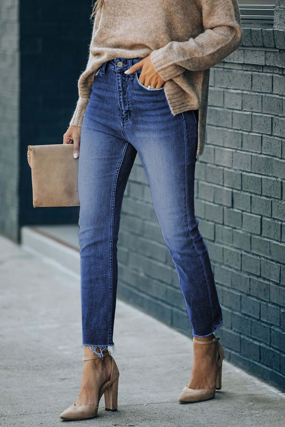 Woman wearing High Waist Raw Hem Skinny Jeans with pockets, paired with a beige sweater and nude heels, standing outdoors.