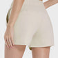 Woman wearing Millennia elastic waist active shorts in beige, showcasing the stylish back view and pocket feature.