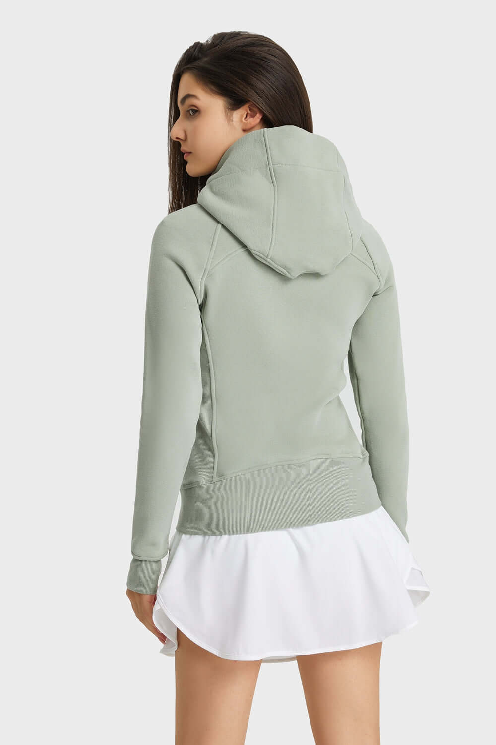 Stylish back view of a woman in a light green hooded sports jacket paired with a white skirt, perfect for outdoor activities.