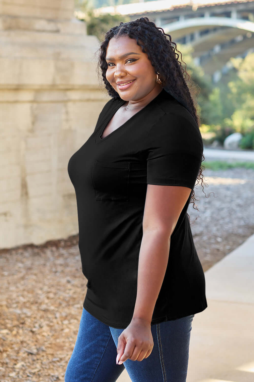 Woman wearing Basic Bae Bamboo Full Size V-Neck Short Sleeve T-Shirt in black, standing outdoors.