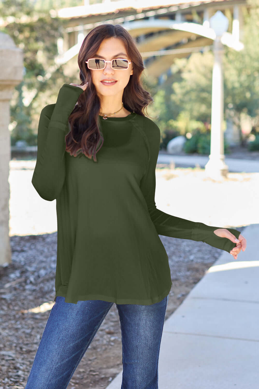 Woman wearing a round neck long sleeve T-shirt in green, paired with blue jeans, outdoors.