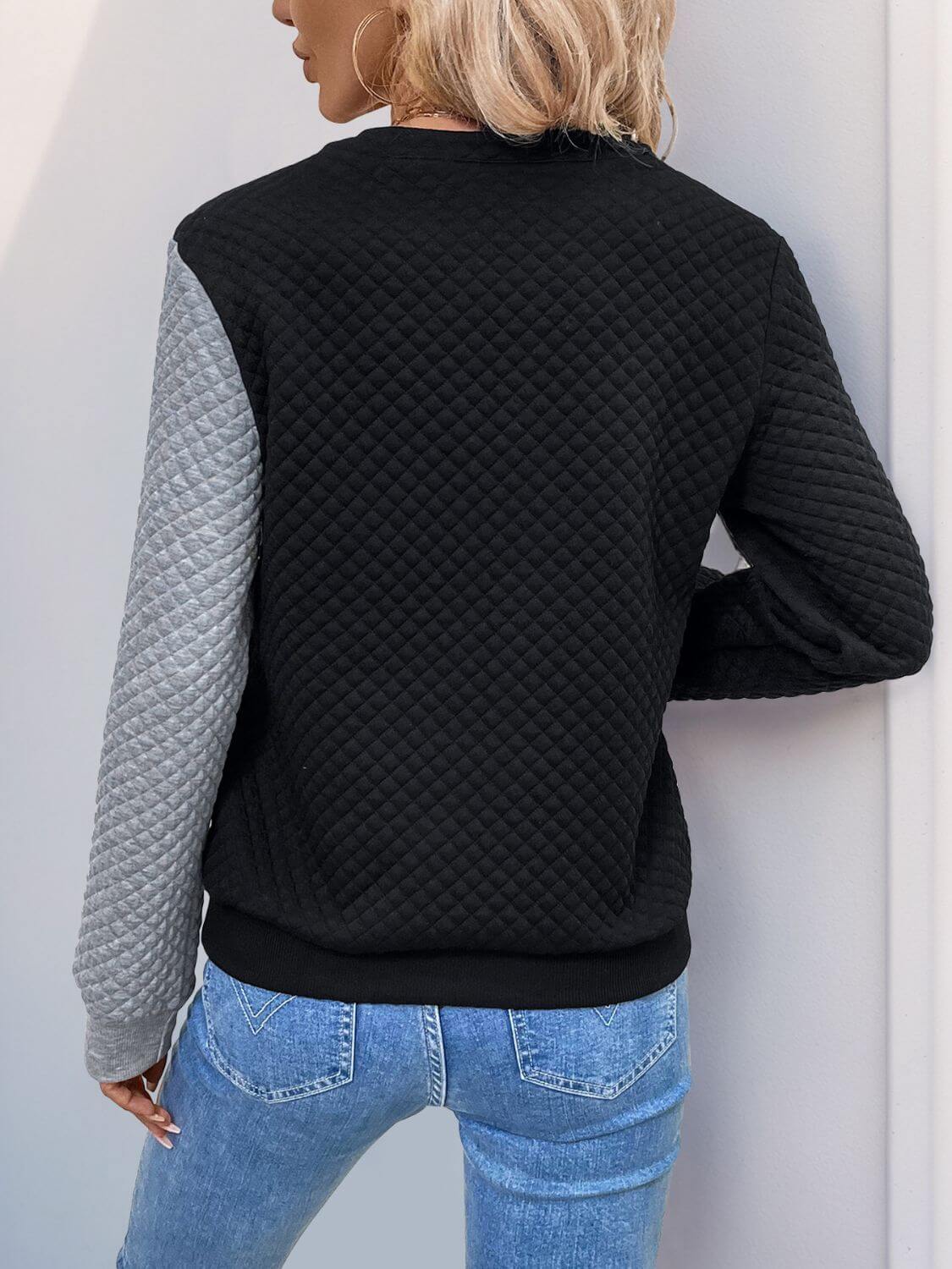 Woman in black decorative button contrast long sleeve sweatshirt with quilted design and grey sleeve, standing outdoors.