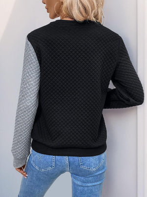 Woman in black decorative button contrast long sleeve sweatshirt with quilted design and grey sleeve, standing outdoors.