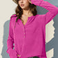 Woman wearing a pink long sleeve notched thumbhole t-shirt with buttons, paired with a straw hat and white pants.