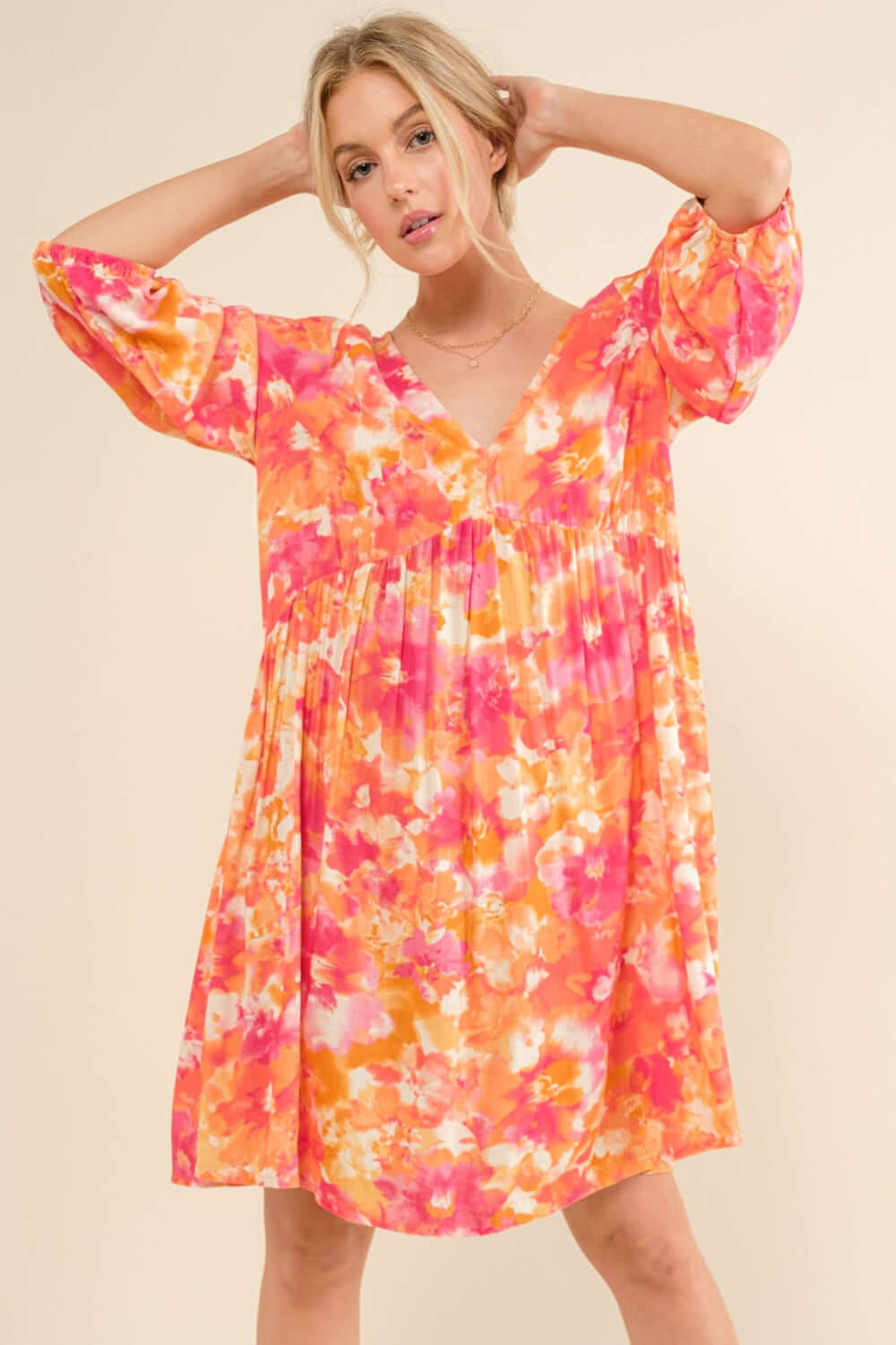 Woman wearing a vibrant orange and pink floral printed dress with puffy sleeves and a V-neckline.