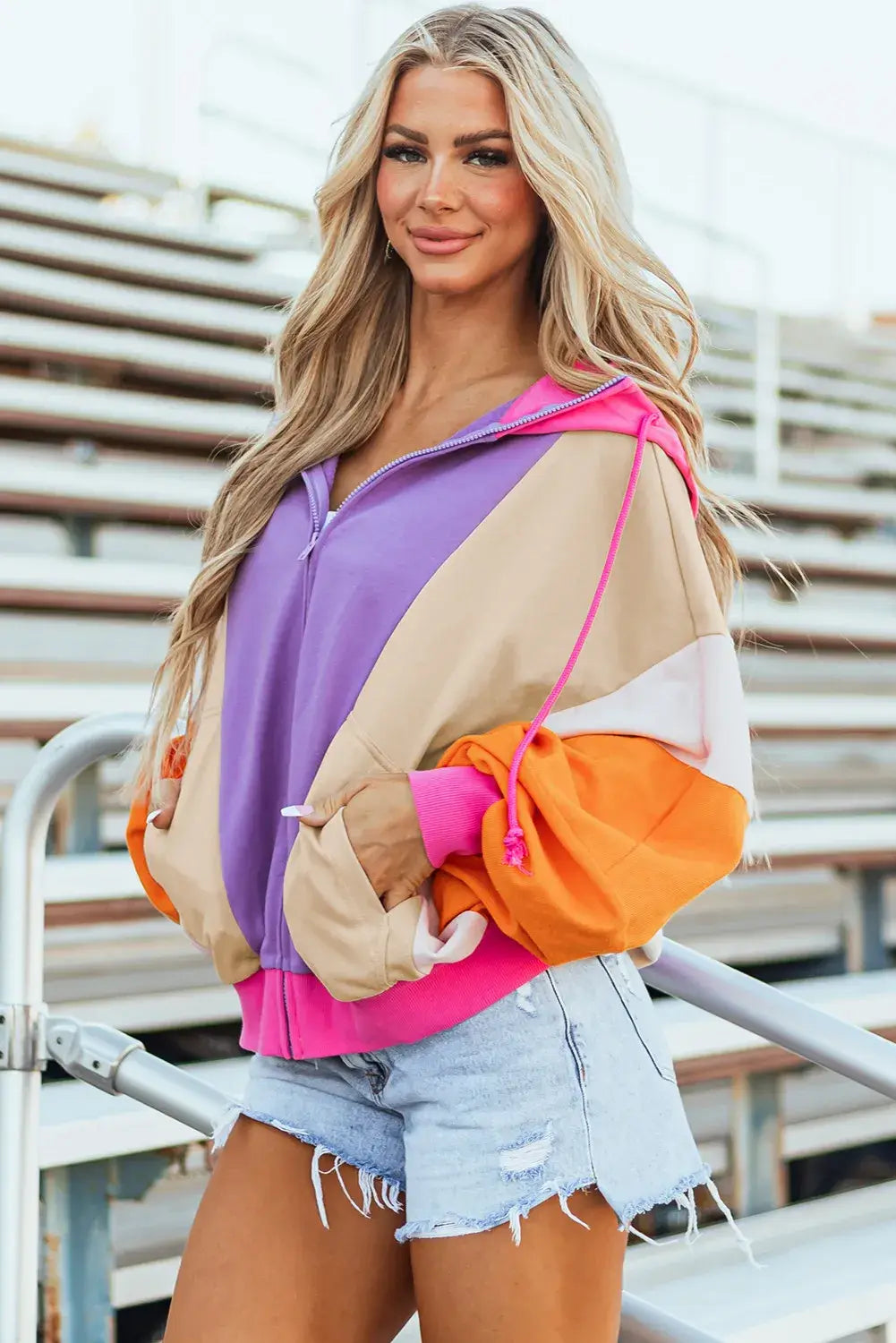 Woman wearing drawstring color block zip up long sleeve hoodie with vibrant colors and denim shorts.